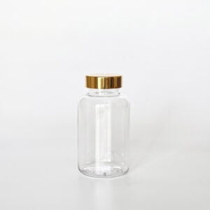 TGPG-200，透明亮金蓋200ml PETG錠劑瓶，是由透明的PETG塑膠瓶上面搭配38mm的金色電鍍瓶蓋，電鍍金蓋裡面含有墊片，可選配感壓封口紙，整組瓶子直立於一張白色背景上。此塑膠容器通常用於保健食品、醫療藥品、健康食品、分裝藥瓶、藥罐或是寵物用藥品身上。